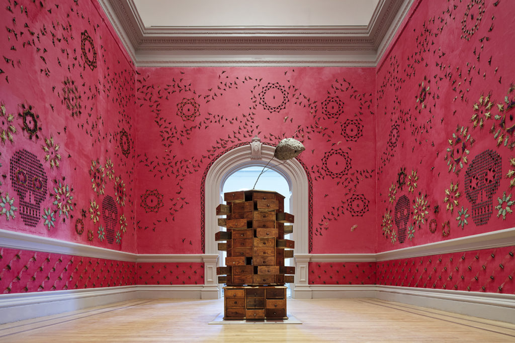 A stack of drawers stand in the middle of a pink room with skull decor