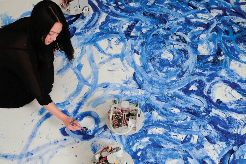 A painter uses a brush on a canvas on her floor