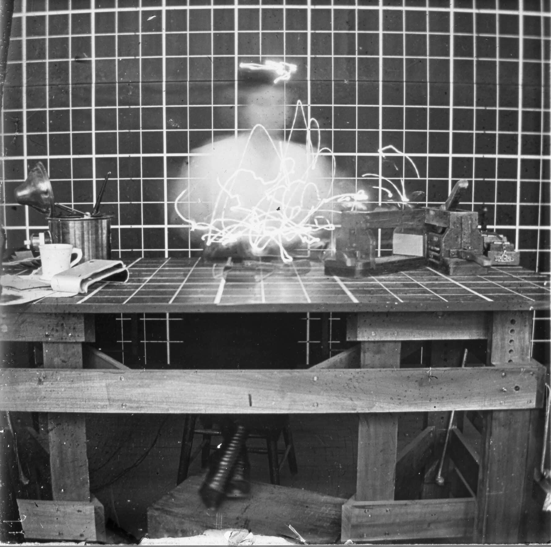 Frank and Lillian Gilbreth, Cyclegraph of female at gridded table and gridded background.
Table height is adjustable and her feet are on a box.